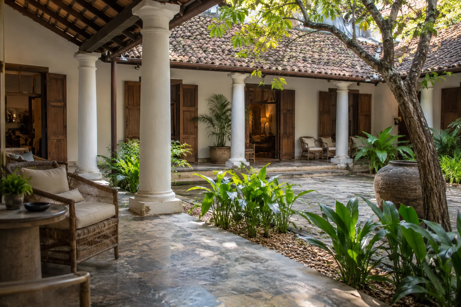 Shaded heritage courtyard with white columns, timber shutters and rattan seating